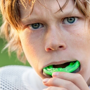 Young boy putting a green athletic mouthguard in his mouth