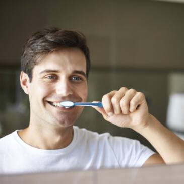 Smiling man brushing his teeth in front of a mirror