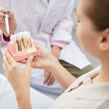 Dentist showing a patient a model of a dental implant in the jaw