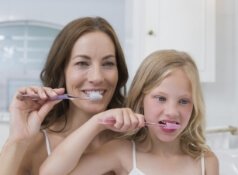 Mother and young daughter brushing their teeth together