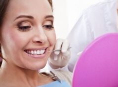 Woman in dental chair looking at her teeth in a pink hand mirror