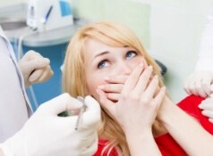 Young woman covering her mouth with her hands and looking scared in dental chair