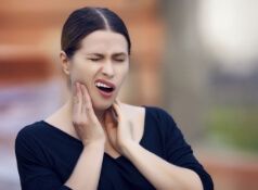 Woman in navy blue blouse holding her face in pain